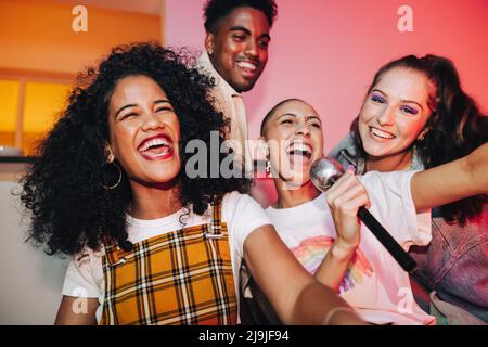 De jeunes amis chantent leur chanson préférée pendant la soirée karaoké. Des amis heureux qui rient avec joie lors d'une fête à la maison. Groupe d'amis multiculturels havi Banque D'Images