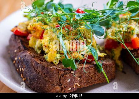 Petit déjeuner sandwich avec œufs brouillés. Sandwichs cuits avec œufs, fromage, tomates, poivrons rouges et petits pois sur une assiette. Gros plan omel Banque D'Images