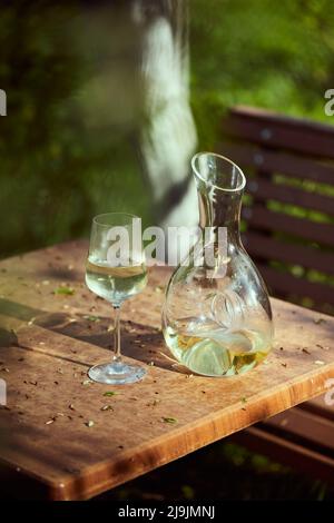 Verre et carafe au vin blanc sur une table dans le jardin. Une soirée de printemps entourée par la nature. Photo verticale. Banque D'Images