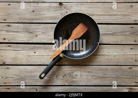 Une poêle et une spatule en bois avec les restes de nourriture frite sur une table en bois à la maison dans la cuisine, vaisselle sale, une vieille poêle Banque D'Images
