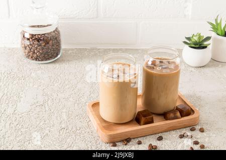 deux verres modernes en forme de boîte de café latte froid, une boisson au chocolat ou mocha sur un plateau en bois face d'un mur de briques blanches Banque D'Images