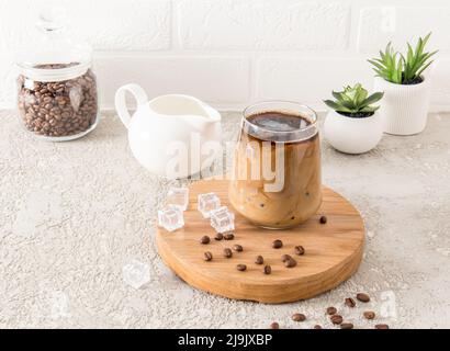 un café de dalgona froid avec des glaçons dans un grand verre sur un panneau rond en bois et un fond gris ciment. super boisson d'été Banque D'Images