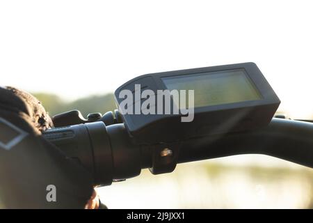 une main femelle dans un gant noir tient le volant d'un e-bike au soleil dans le parc, conduisant un e-bike, se reposant sur un vélo Banque D'Images