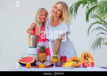 famille caucasienne dans la cuisine pendant le petit déjeuner à la maison. deux sœurs blondes cuisant des smoothies dans un mélangeur.thème tropical d'été.petit veg d'affaires Banque D'Images