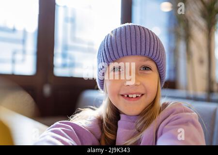 Un enfant qui montre une dent de lait manquée. Changer de concept de dents. Jolie petite fille caucasienne aux cheveux blonds de huit ans dans un café moderne. Couleur tendance de 2022 Banque D'Images