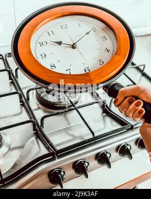 Une main femelle tient la poignée d'une poêle avec une horloge murale à l'intérieur, comme elle la met sur la cuisinière Banque D'Images