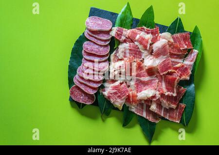 Fuet, saucisse tranché et jambon espagnol ibérique sur fond vert. Saucisse espagnole. Gastronomie et gastronomie en Espagne. Jambon traditionnel espagnol Jamon Serrano. Banque D'Images