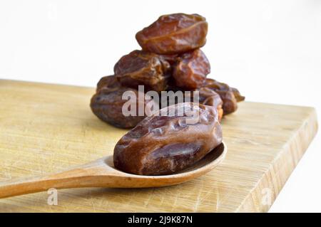 Le hurma frais bio nutritif séché date medjool grains, dans une cuillère en bois sur la planche à découper Banque D'Images