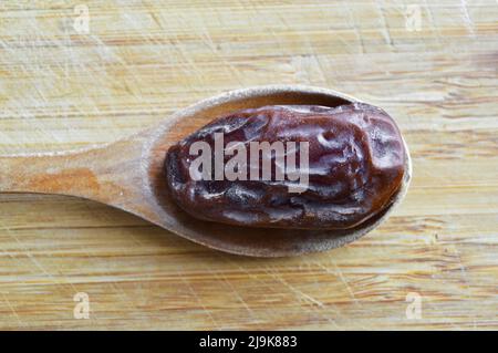 Le hurma frais bio nutritif séché date medjool grains, dans une cuillère en bois sur la planche à découper Banque D'Images