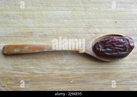 Le hurma frais bio nutritif séché date medjool grains, dans une cuillère en bois sur la planche à découper Banque D'Images