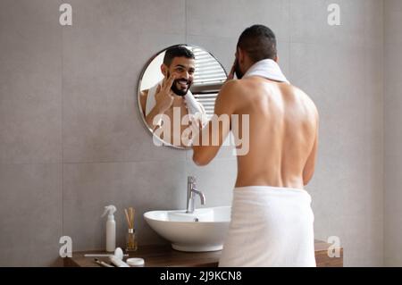 Joyeux gars regardant dans le miroir mettant la crème sur le visage Banque D'Images