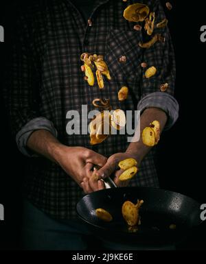 Bratkartoffeln allemand ou pommes de terre frites jetant par l'air du chef de cuisine sur fond noir Banque D'Images