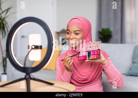 Blog beauté réussi. Bonne dame enregistrant l'examen des produits cosmétiques, montrant la palette de rouge à lèvres au téléphone cellulaire Banque D'Images