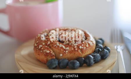 Gros plan d'un rouleau de cannelle et de bleuets autour d'elle sur une assiette en bois avec une fourchette à côté dans un cadre lumineux et lumineux Banque D'Images