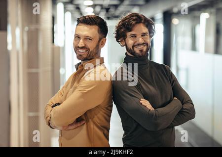 Portrait de deux hommes d'affaires heureux debout avec des bras croisés, souriant à la caméra dans le hall d'entreprise moderne Banque D'Images