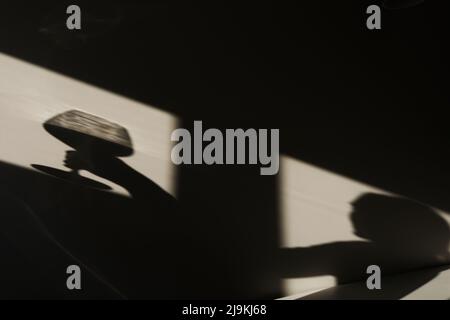 Ombre sur le mur d'un sommelier féminin avec un verre de vin. Silhouette d'une fille qui boit du vin. Chiaroscuro de la fenêtre Banque D'Images