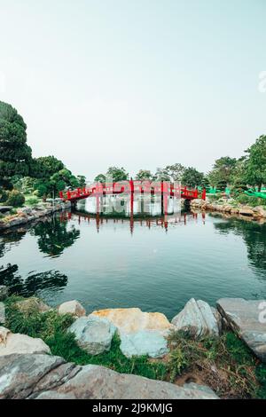 Pont rouge dans un parc de jardin japonais avec un lac entouré de rochers comme décoration et un pont japonais emblématique rouge vif Banque D'Images