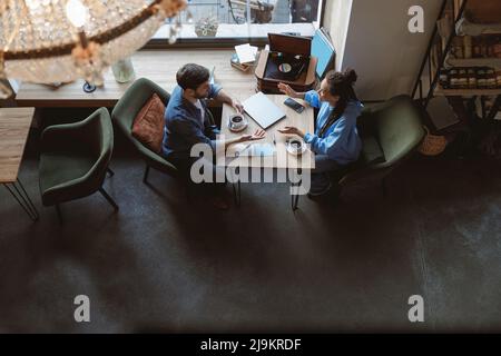 Vue d'en haut sur les courses mixtes de jeunes amis ou collègues qui parlent à table avec un café dans le café. Banque D'Images