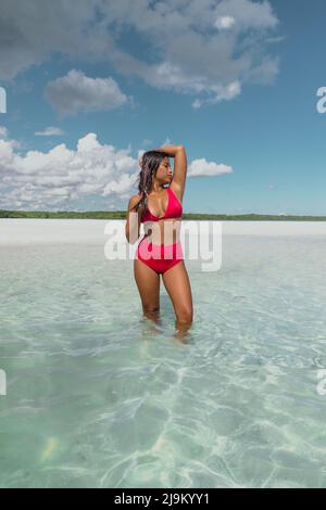 Jeune femme asiatique Havane avec de longs cheveux foncés et un maillot de bain rouge debout dans l'océan bleu turquoise sur l'île privée de Leebong avec plage de sable blanc Banque D'Images