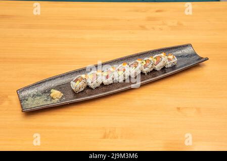 Plateau noir de style moderne avec une portion de sushi uramaki au saumon avec avocat, œufs de macago, algues nori, riz japonais, graines de sésame et de pavot, gingembre A. Banque D'Images