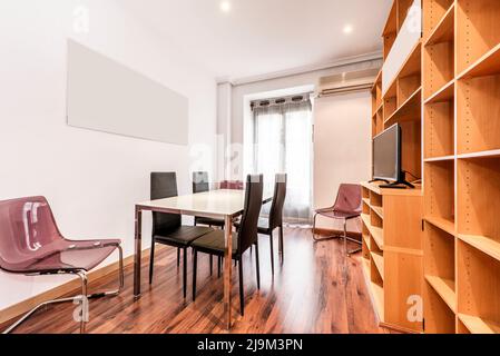 Bureau professionnel avec table de réunion en verre et en métal chromé avec chaises en similicuir noir, étagères en bois à compartiments multiples, parquet et baie Banque D'Images