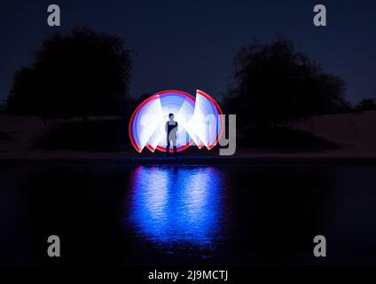 Un tableau lumineux coloré d'un homme habillé comme un astronaute avec des lumières LED multicolores qui jettent de magnifiques reflets dans l'eau Banque D'Images
