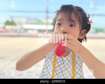 mignonne petite fille essaie de gonfler un ballon Banque D'Images