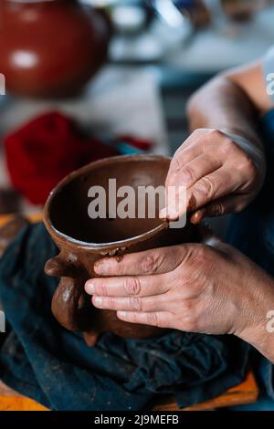 Clamant féminin non reconnaissable Clamant ceramist en tablier façonnant morceau de pot d'argile en main dans l'atelier Banque D'Images