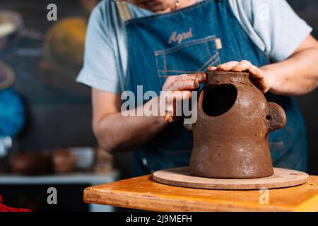 Clamant féminin non reconnaissable Clamant ceramist en tablier façonnant morceau de pot d'argile en main dans l'atelier Banque D'Images