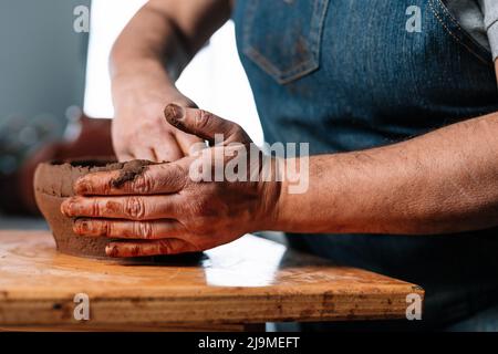 Clamant féminin non reconnaissable Clamant ceramist en tablier façonnant morceau de pot d'argile en main dans l'atelier Banque D'Images