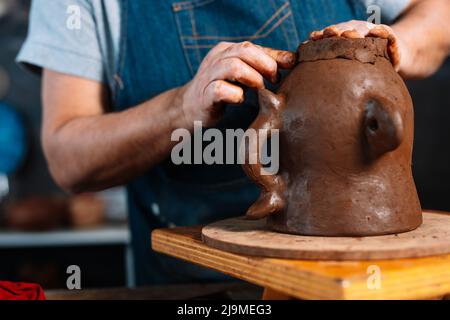 Clamant féminin non reconnaissable Clamant ceramist en tablier façonnant morceau de pot d'argile en main dans l'atelier Banque D'Images