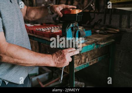 Vue latérale d'un mécanicien masculin non reconnaissable court à l'aide d'un tournevis et en réparant l'ancien phare du tracteur en travaillant dans un garage en rade Banque D'Images