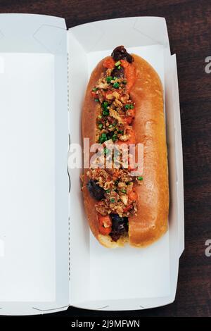 Vue de dessus d'un délicieux hot dog avec saucisse et garniture d'oignon frit servi dans une boîte en papier au restaurant Banque D'Images