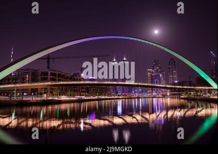 Belle vue sur le pont de tolérance illuminé avec Skysrcapers en arrière-plan et la pleine lune capturée la nuit depuis le canal de Dubaï Banque D'Images