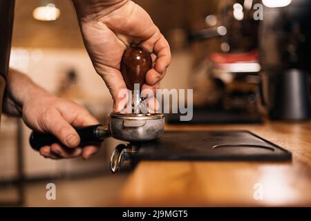 Vue latérale de la récolte un barista masculin méconnaissable prépare du café moulu avec un porte-filtre inviolable en se tenant au comptoir dans le café Banque D'Images