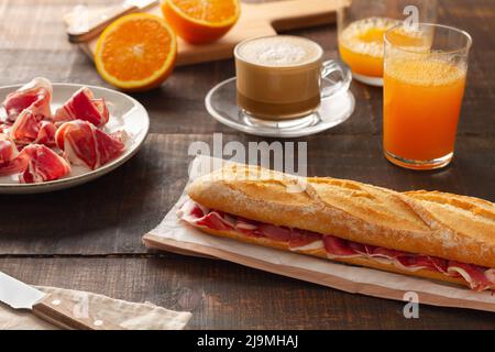 Du dessus du sandwich avec du jambon sur le sac en papier placé près d'un verre de jus d'orange et d'une tasse de café Banque D'Images