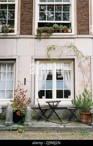 De petites chaises en bois et une table sont placées sur le trottoir près de la fenêtre du vieux bâtiment en briques dans le quartier d'Amsterdam Banque D'Images