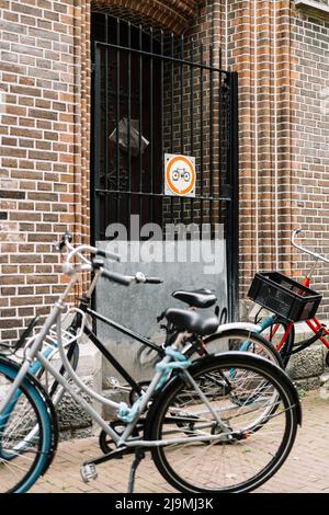 Divers vélos modernes garés près de la clôture d'un bâtiment en briques dans la rue d'Amsterdam en journée Banque D'Images