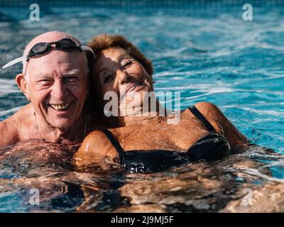 Joyeux couple senior souriant avec éclat tout en nageant ensemble dans la piscine extérieure pendant les vacances d'été Banque D'Images