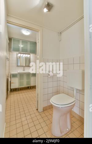 toilettes en céramique blanche placées au mur carrelé dans la salle de bains avec lavabo et armoires Banque D'Images