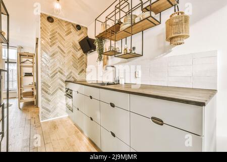 Moderne lumière armoires de cuisine élégantes avec mur de carrelage un évier placé au mur avec diverses fournitures sur des étagères dans l'appartement Banque D'Images