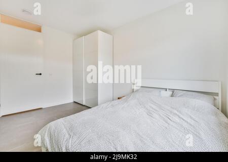 Lit confortable avec couette et oreiller près de la porte blanche et placard blanc dans la chambre lumineuse de la maison Banque D'Images