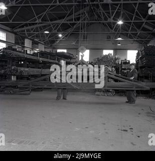 1950s, historique, deux hommes supervisant le déplacement de tiges d'acier sur un harnais de levage industriel Morris de 2 tonnes à l'intérieur d'un hangar industriel de la Steel Company of Wales, Abbey Works, Port Talbot, pays de Galles, Royaume-Uni. Le harnais de levage de l'industrie lourde a été fabriqué par Herbert Morris Ltd de Loughborough, une entreprise britannique d'ingénierie prospère qui a fabriqué des grues et des ascenseurs et qui avait été établi en 1864. Banque D'Images