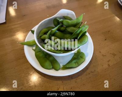 Gros plan, accent sélectif sur les gousses d'edamame dans une petite tasse blanche sur une table en bois à l'intérieur d'un restaurant Banque D'Images