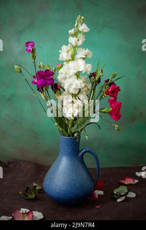 Les fleurs de Dianthus sont aussi appelées "pinks" et Matthiola incana dans un vase en céramique bleu sur une table en cuir brun Banque D'Images