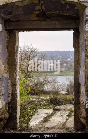 Porte sans porte de vieille maison en ruine. Vue sur les arbres, la rivière, le village et le ciel gris fumé. Gros plan. Mise au point sélective. Copier l'espace. Banque D'Images