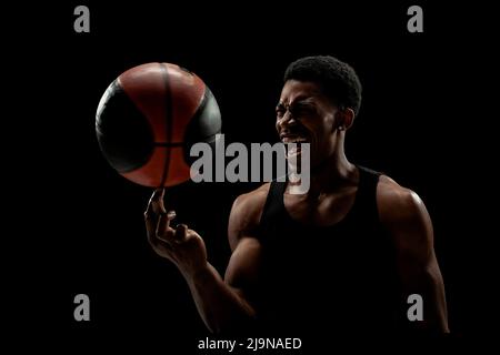 Joueur de basket-ball tournant une balle sur fond noir. Hurlant la silhouette de l'homme afro-américain. Banque D'Images