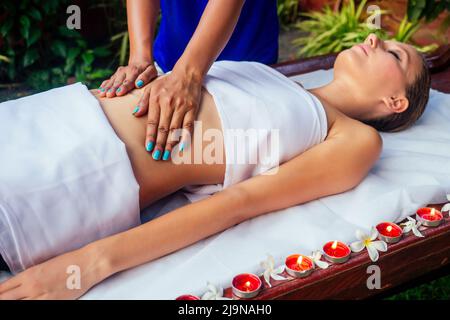 Mains massant l'abdomen de la femme.thérapeute appliquant des bougies de pression et des fleurs sur le fond Banque D'Images