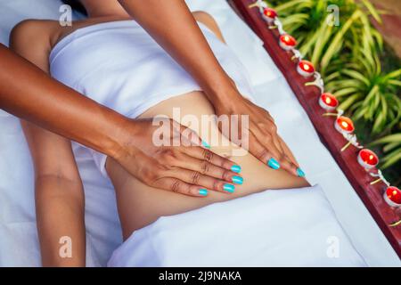 Mains massant l'abdomen de la femme.thérapeute appliquant des bougies de pression et des fleurs sur le fond Banque D'Images