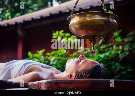 Massage ayurveda thérapie de guérison alternative.belle femme caucasienne obtenir traitement shirodhara est posé sur une table en bois salon en Inde Banque D'Images